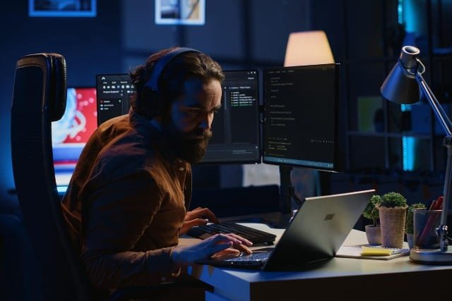 Clevo PA71 A man with a beard and headphones is focused on his Clevo PA71 laptop, working intently.