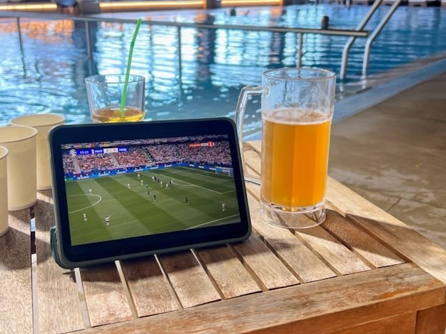 A tablet with a soccer match on Crackstreams 2.0 rests on a table next to a pool.