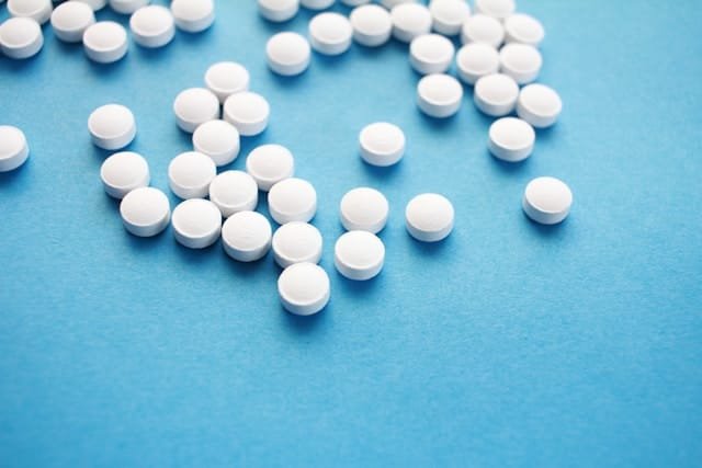 hal-gatewood-nhG5gix93es-unsplash K18 pill white scattered on a blue background, showcasing their smooth surface and round shape.