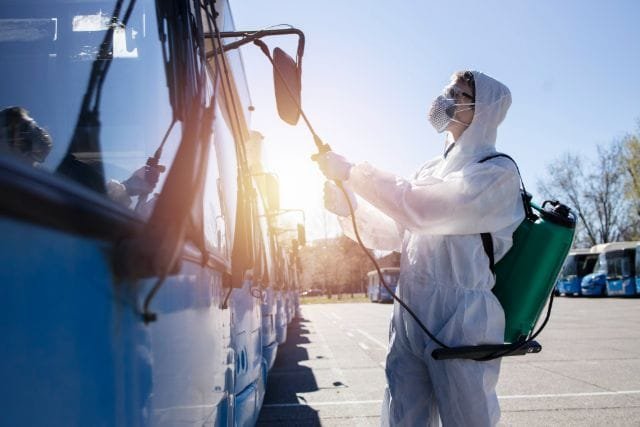 A person in a protective suit sprays a bus for pest control, labeled 