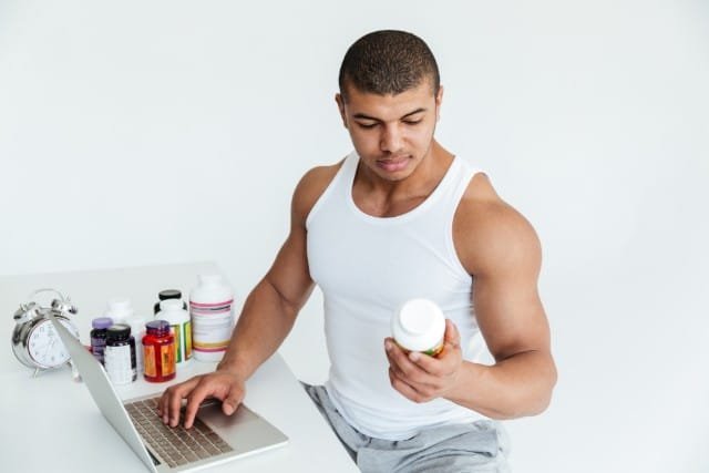 A man sits at a desk with a laptop and pills, reflecting on the impact of steroids on mental health.