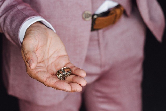 man-pink-suit-holds-two-wedding-rings